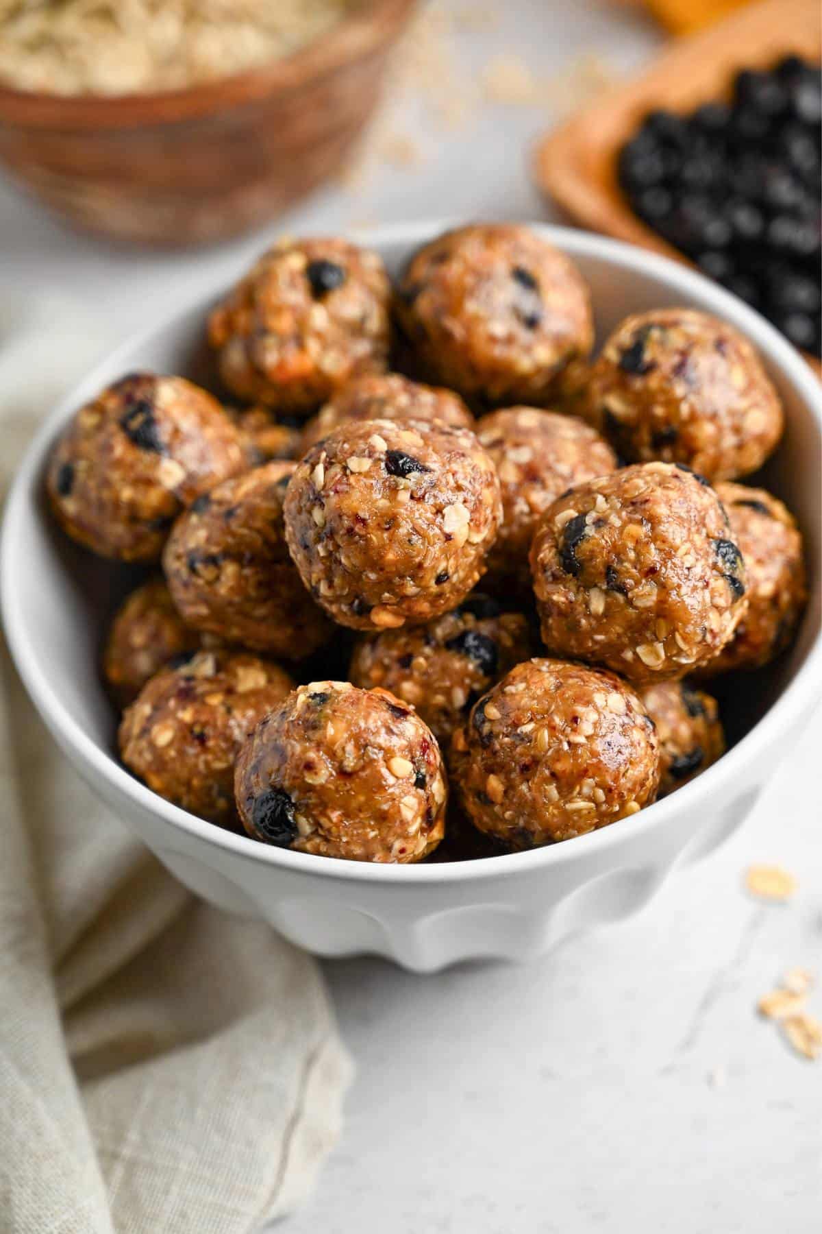a bowl of energy bites with a bowl of oats and dried blueberries