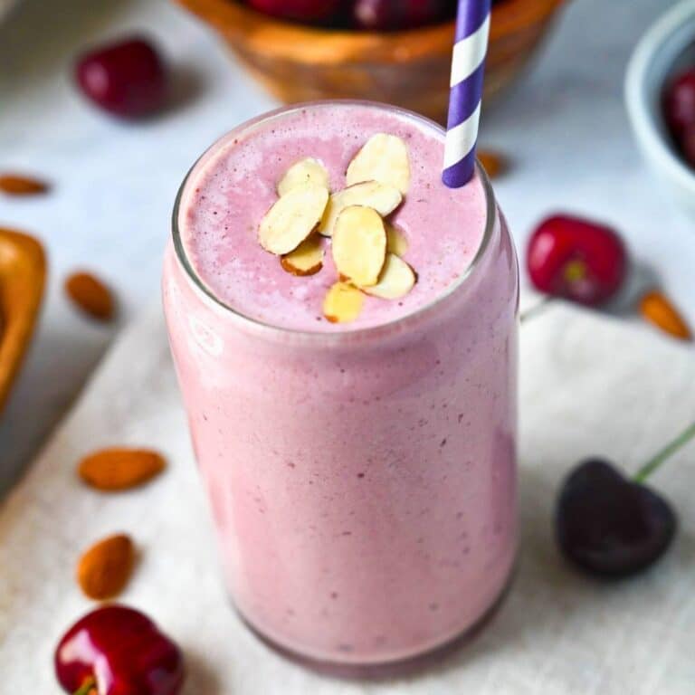 cherry smoothie in a glass with sliced almonds on top and a straw
