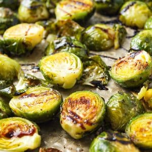 close up of roasted brussels sprouts in bacon grease on a sheet pan with balsamic glaze on top