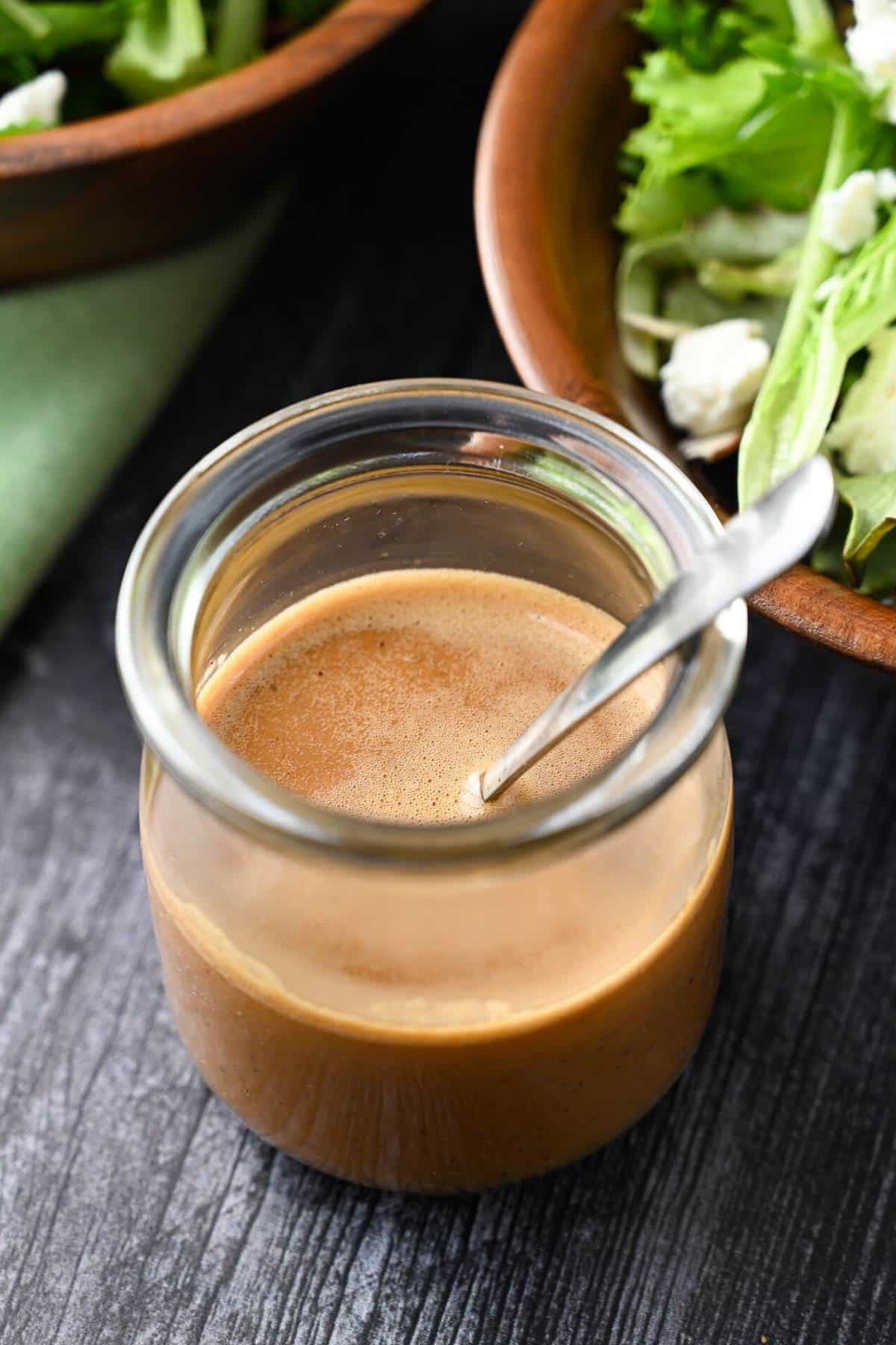 a jar of creamy balsamic dressing with salad bowls behind it
