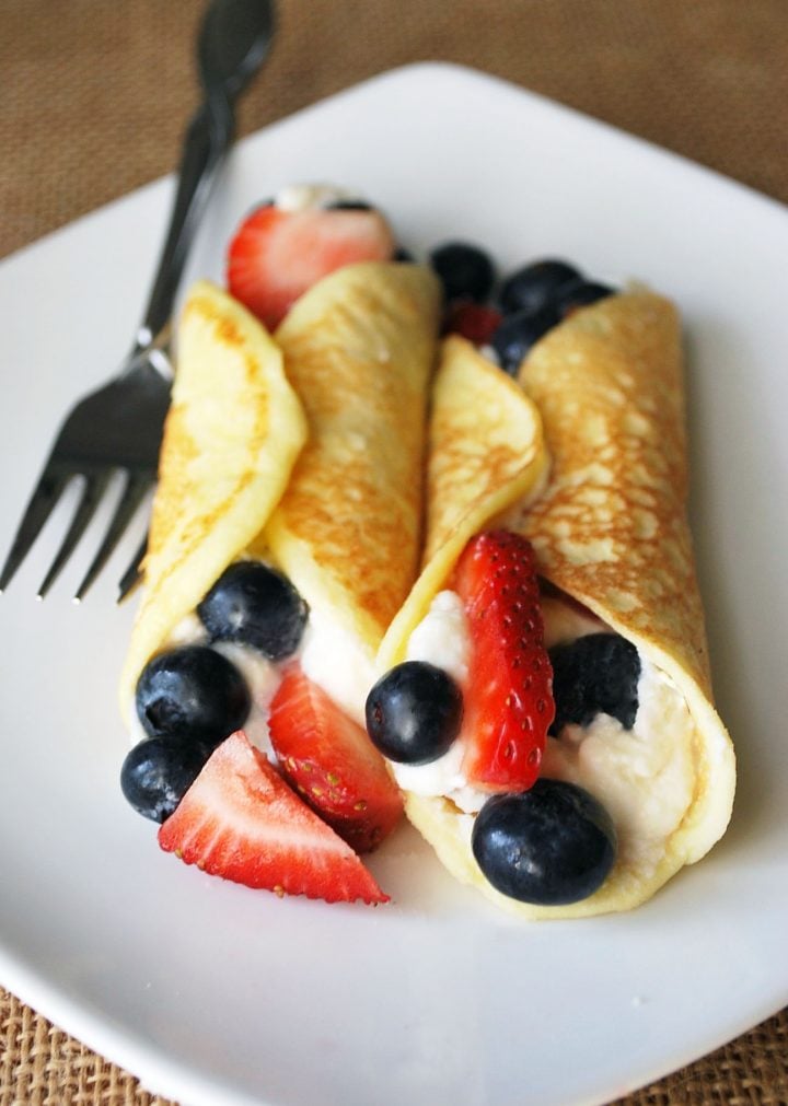 stuffed crepes on a white plate with strawberries and blueberries with fork