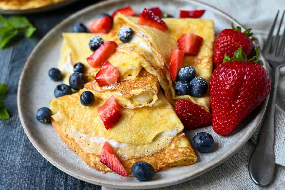 close up photo of a plate of filled cottage cheese crepes with blueberries and strawberries