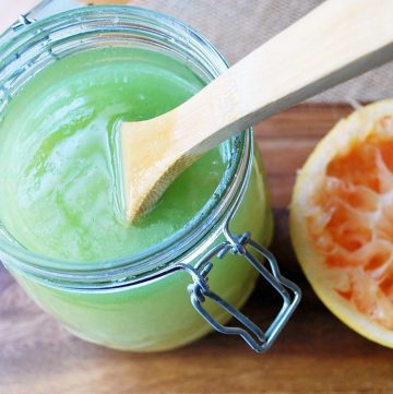 green colored sugar scrub in a jar with a wooden spoon next to a sliced grapefruit