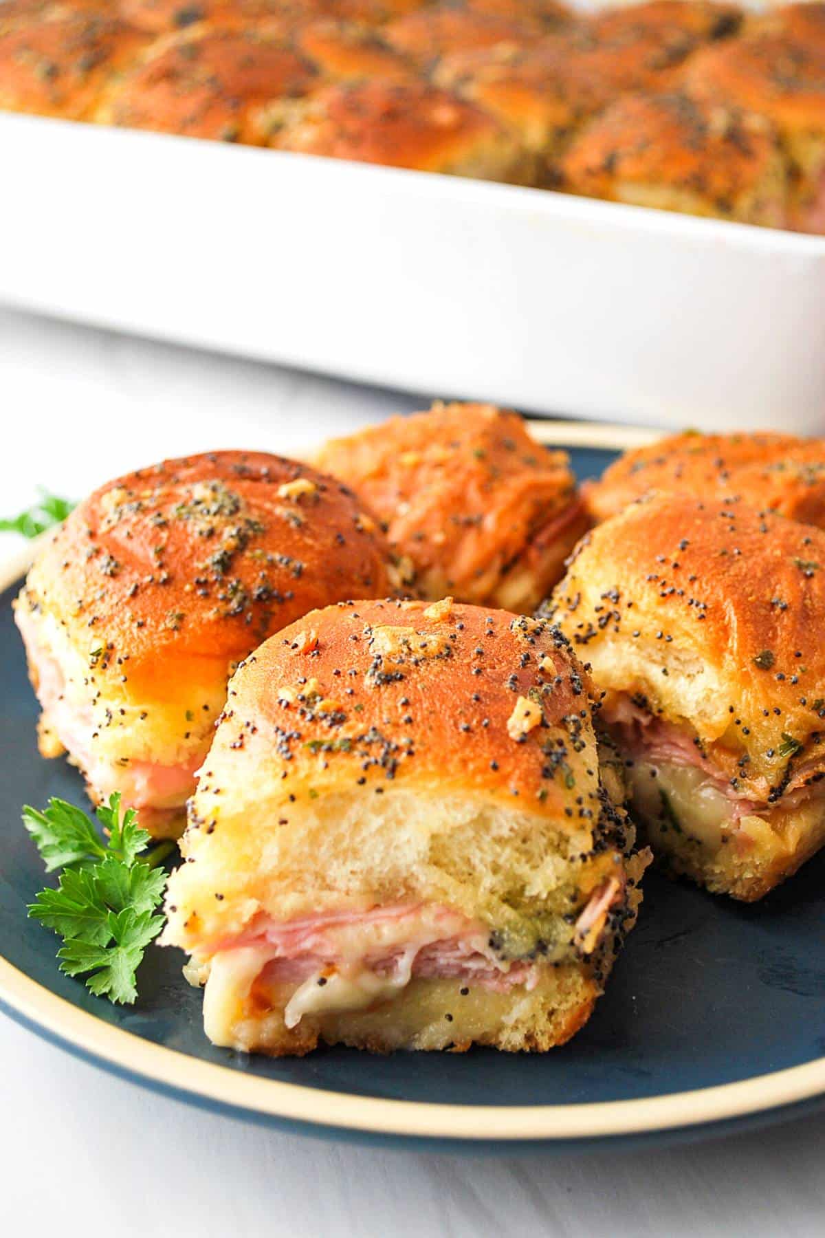 4 baked ham and cheese sliders on a plate with a casserole dish in the background