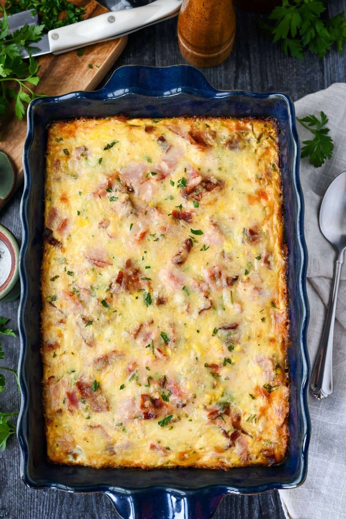 a baked loaded breakfast casserole in a blue 9x13 pan with a napkin and spoon next to it