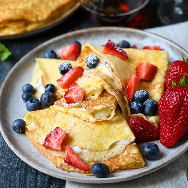crepes filled with a cottage cheese filling topped with berries and powdered sugar on a plate