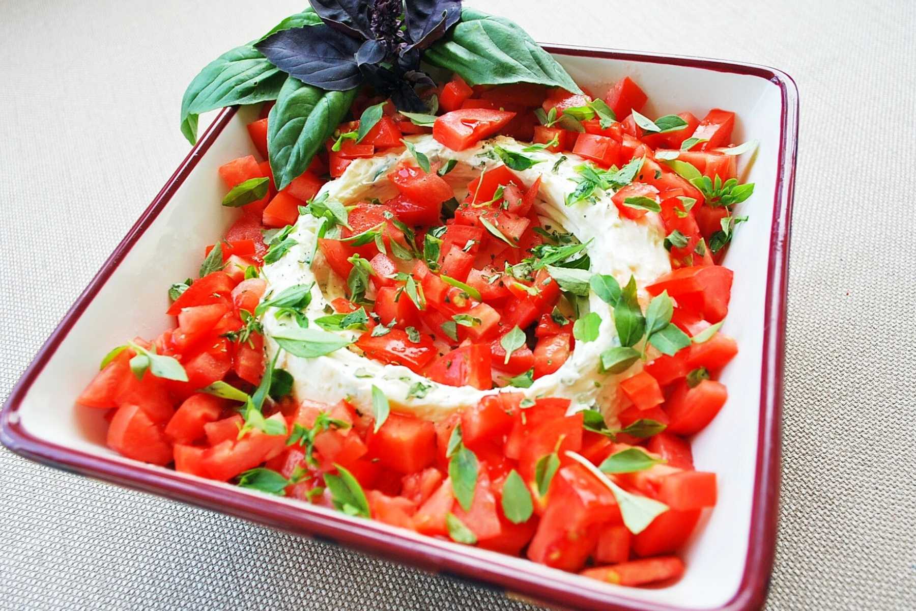 caprese dip in a bowl topped with chopped tomatoes and basil