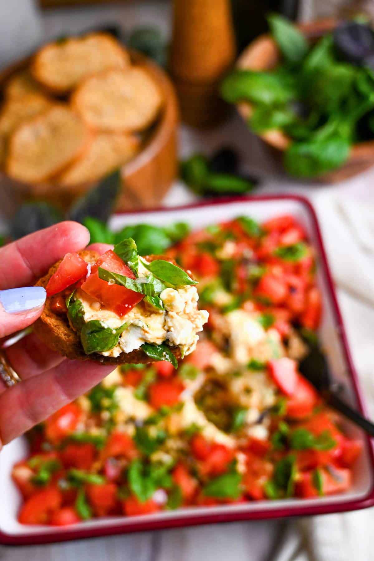 holding up a crostini with caprese dip on it