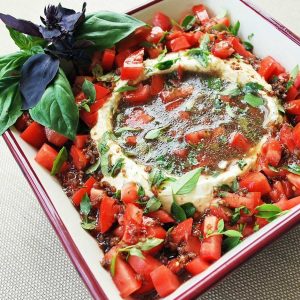 cream cheese dip in a square bowl with a well in the center for the balsamic dressing and chopped tomatoes and basil around the sides