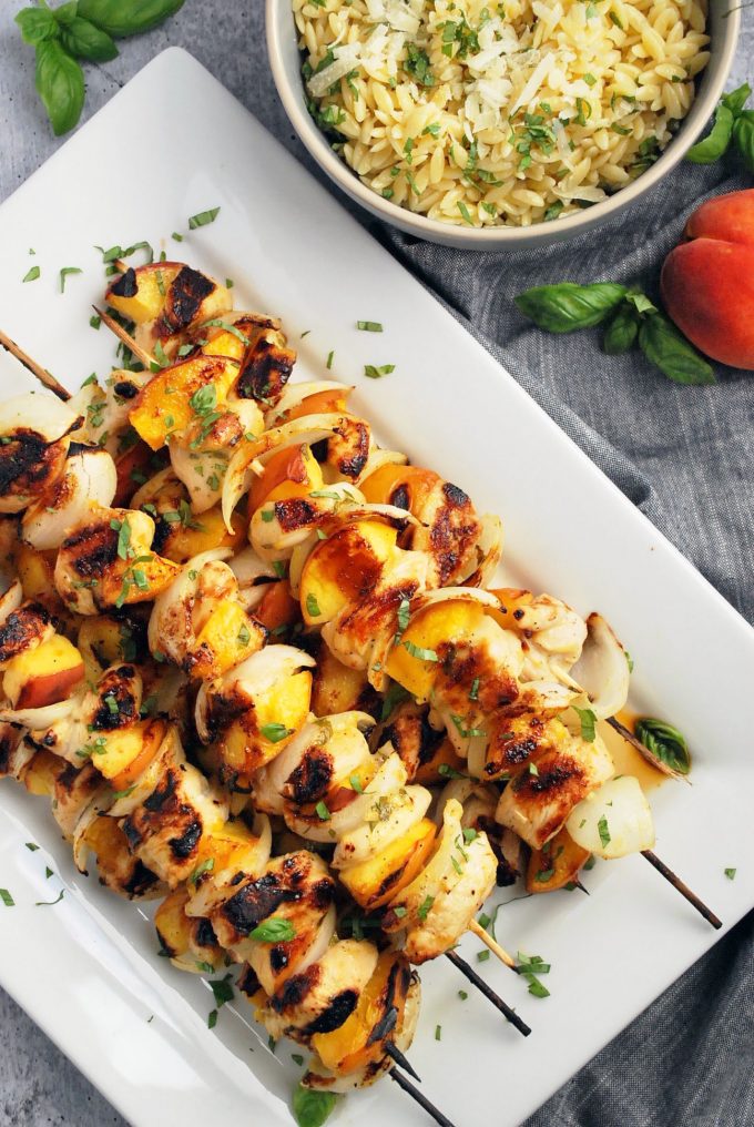 platter of chicken kabobs with onions and peaches garnished with basil