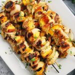 A platter of grilled peach kabobs sprinkled with fresh herbs