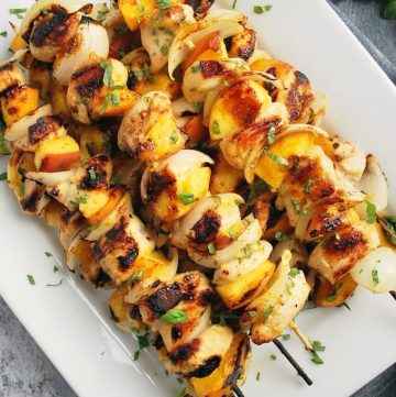 A platter of grilled peach kabobs sprinkled with fresh herbs