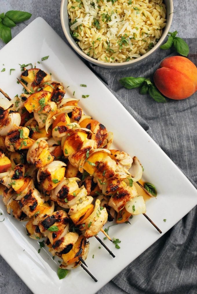 savory peach and chicken kabobs on a platter with a bowl of orzo pasta garnished with fresh basil