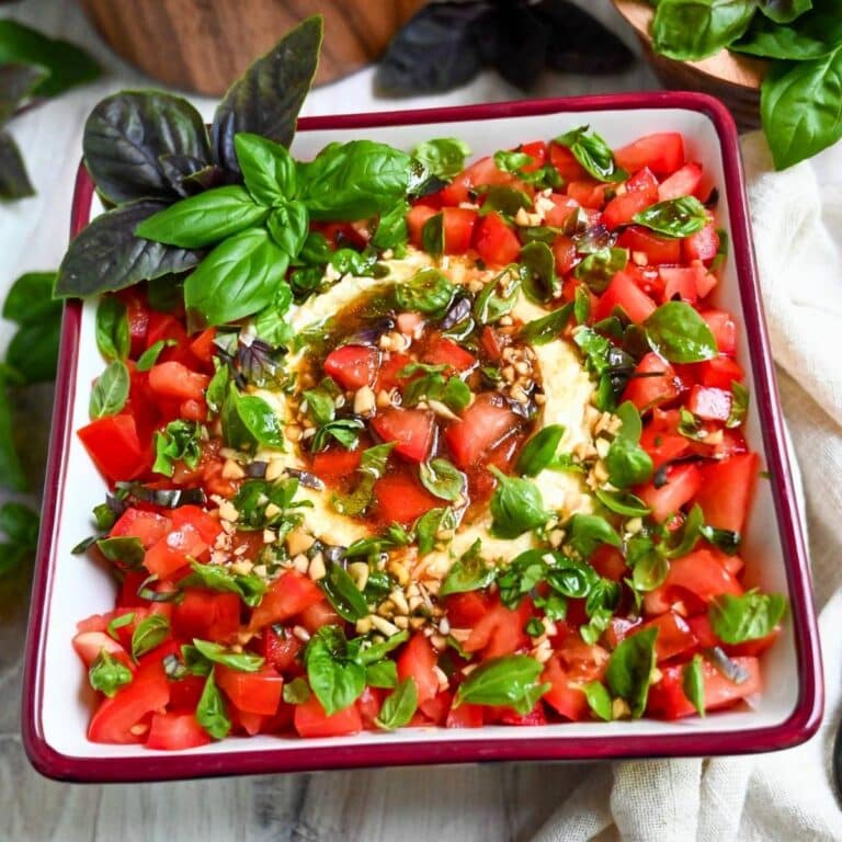 close up of a bowl with a caprese cheese ball and topped with tomatoes, fresh basil and balsamic dressing