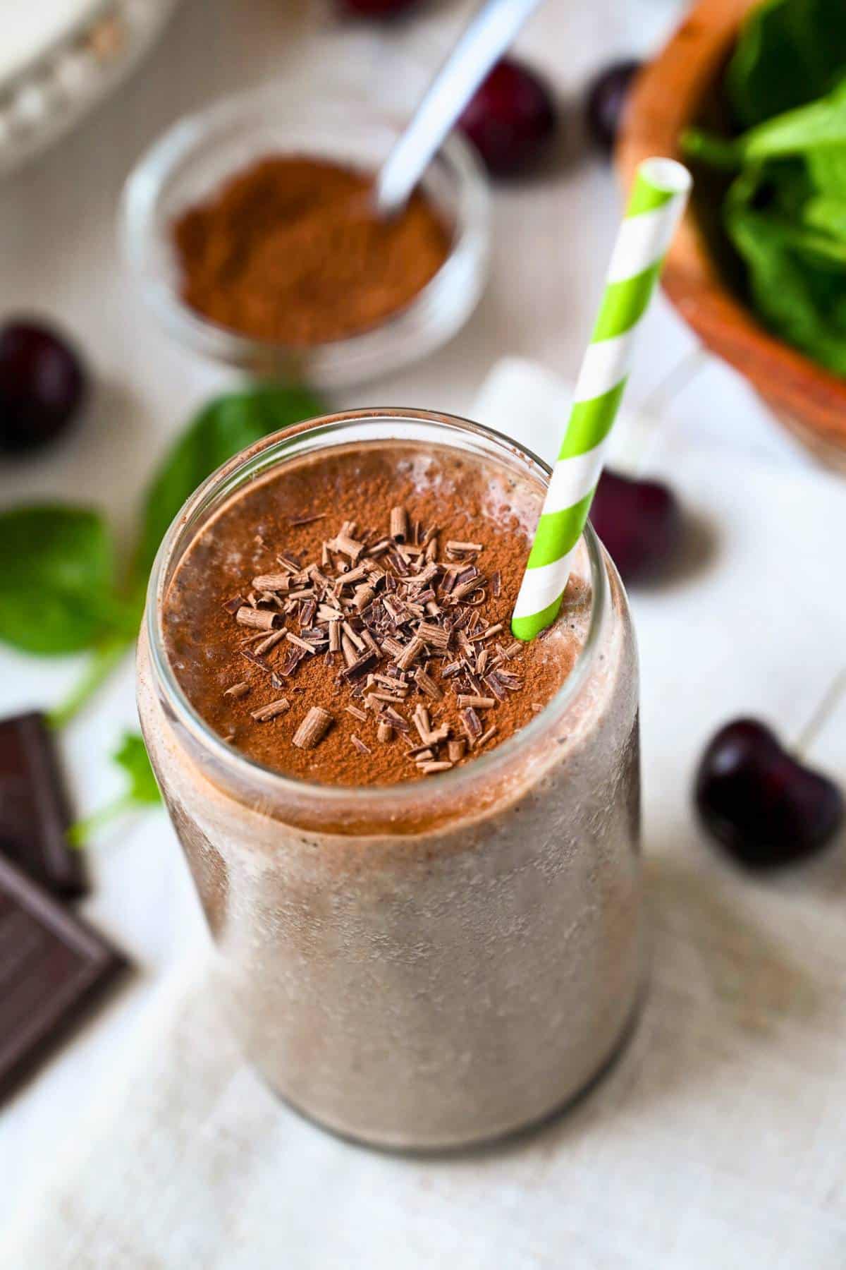 a chocolate cherry smoothie in a glass with cocoa powder and chocolate shavings on top