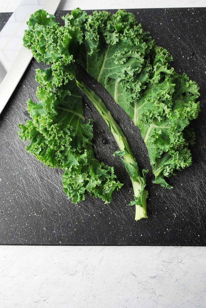cutting kale leaves off the stalk on a cutting board