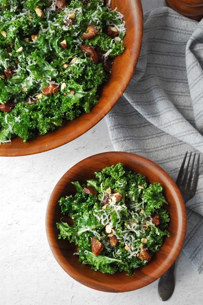 overhead photo of a small and large bowl of kale salad with a napkin and fork on the side