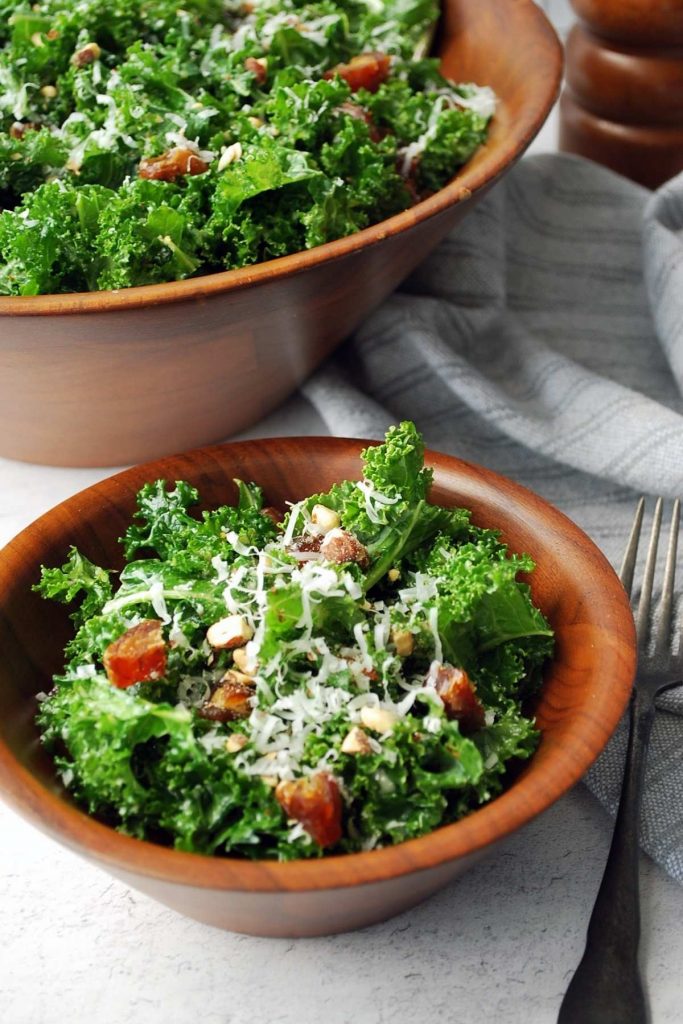 side view of a served bowl of kale salad with a large salad bowl filled with kale salad in the background