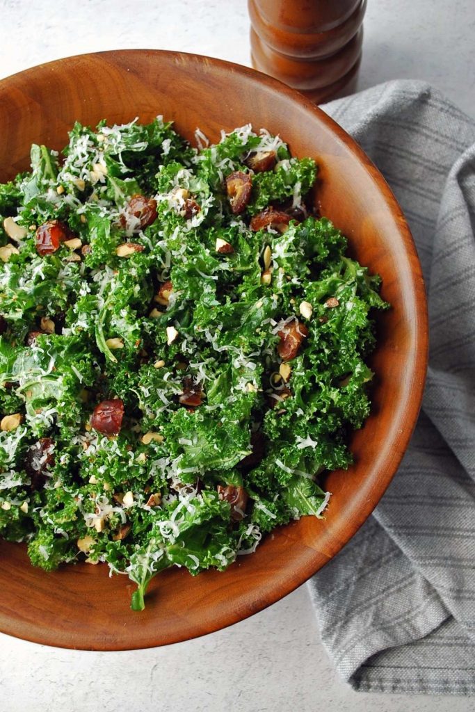 kale salad with dates and parmesan cheese in a large wooden salad bowl