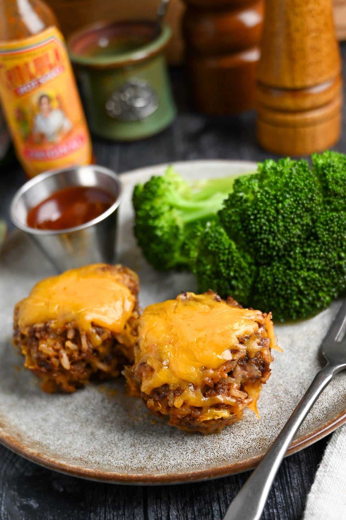 two mini BBQ meatloaves on a plate with cheese on top and broccoli on the side