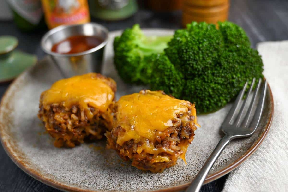 mini meatloaves on a plate topped with cheese with broccoli and a fork