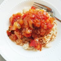 Mango salsa chicken over brown rice in a white bowl with a fork