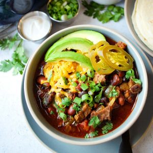 overhead checklist of a bowl of brisket chili topped with cheese, onions, and fresh avocado  Straightforward Dreary Cooker Crimson meat Chili Brisket chili feature  300x300