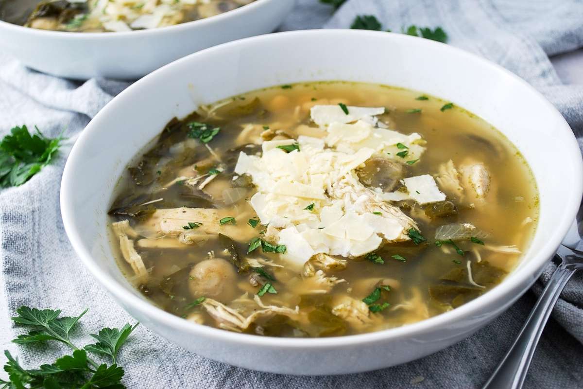 chicken bean soup topped with spinach in a white bowl