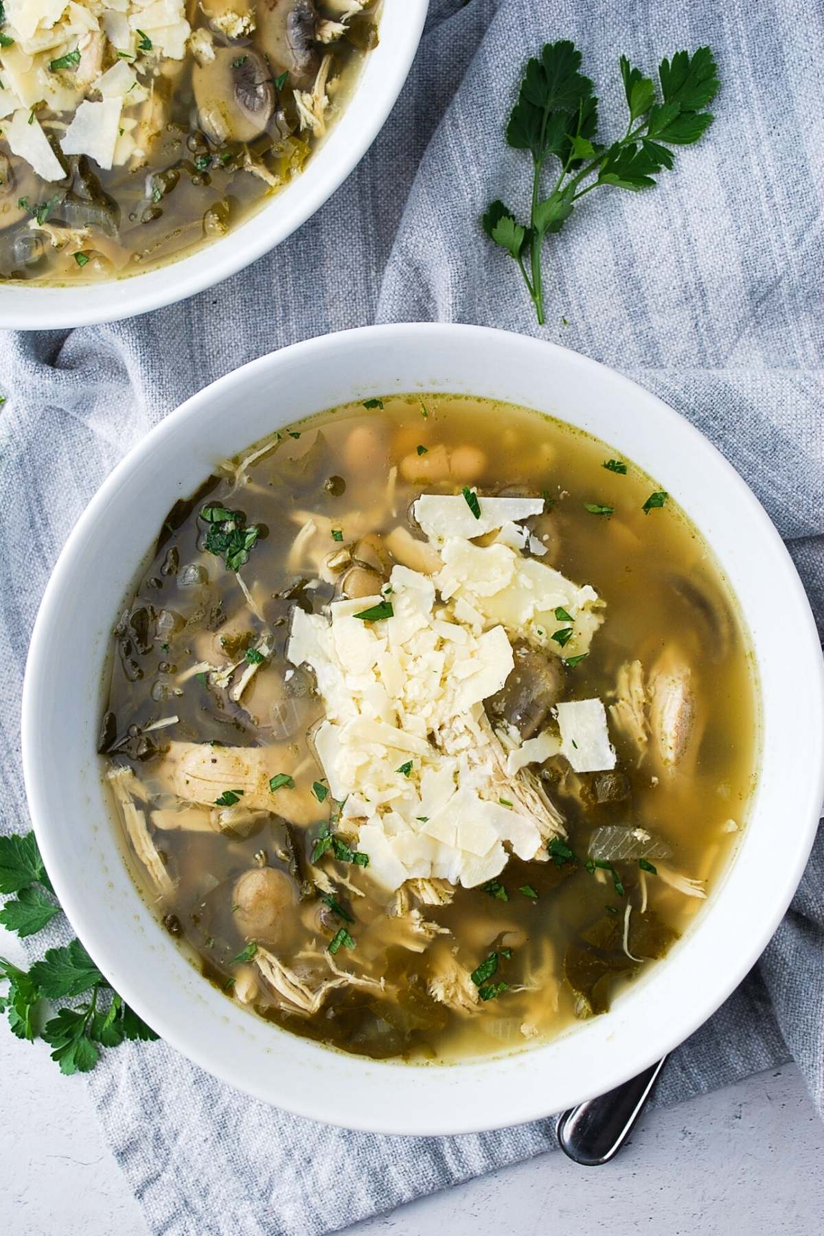 two bowls of chicken bean soup topped with fresh parmesan cheese