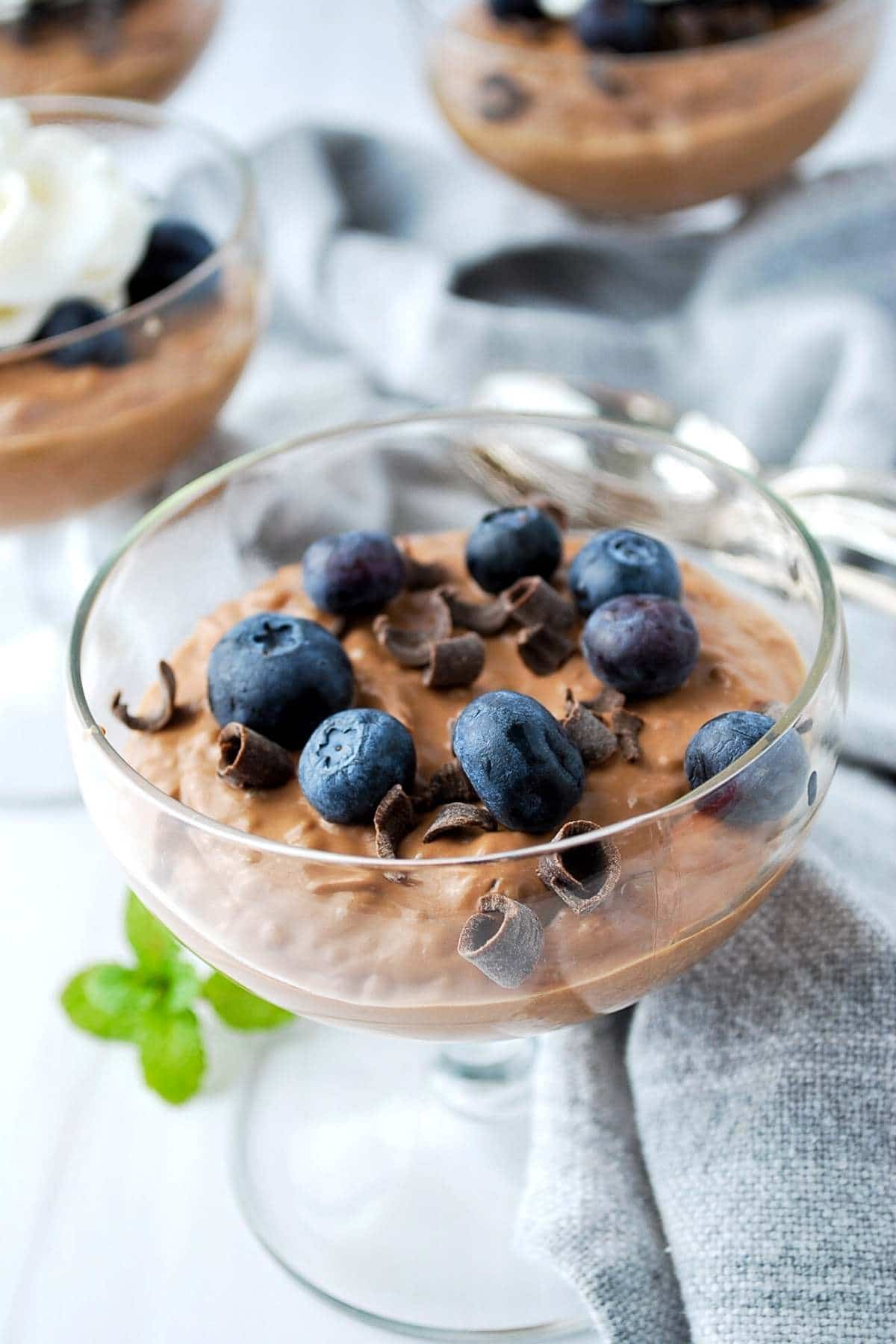 chocolate chia pudding in parfait dishes with blueberries and chocolate shavings