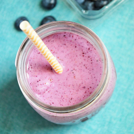 Close up of blueberry smoothie in a glass with yellow and white straw