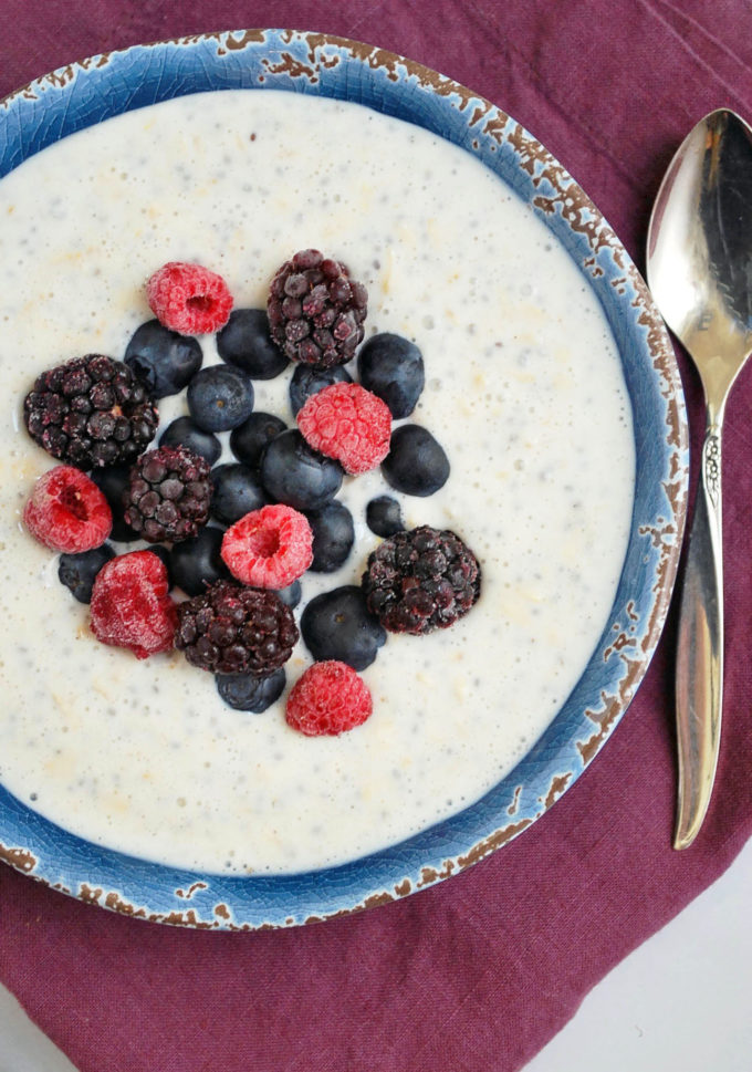 Bowl of overnight Greek yogurt oatmeal with frozen berries on top with a spoon and napkin