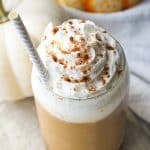 a close up photo of a pumpkin spice latte in a glass with whipped cream and a straw
