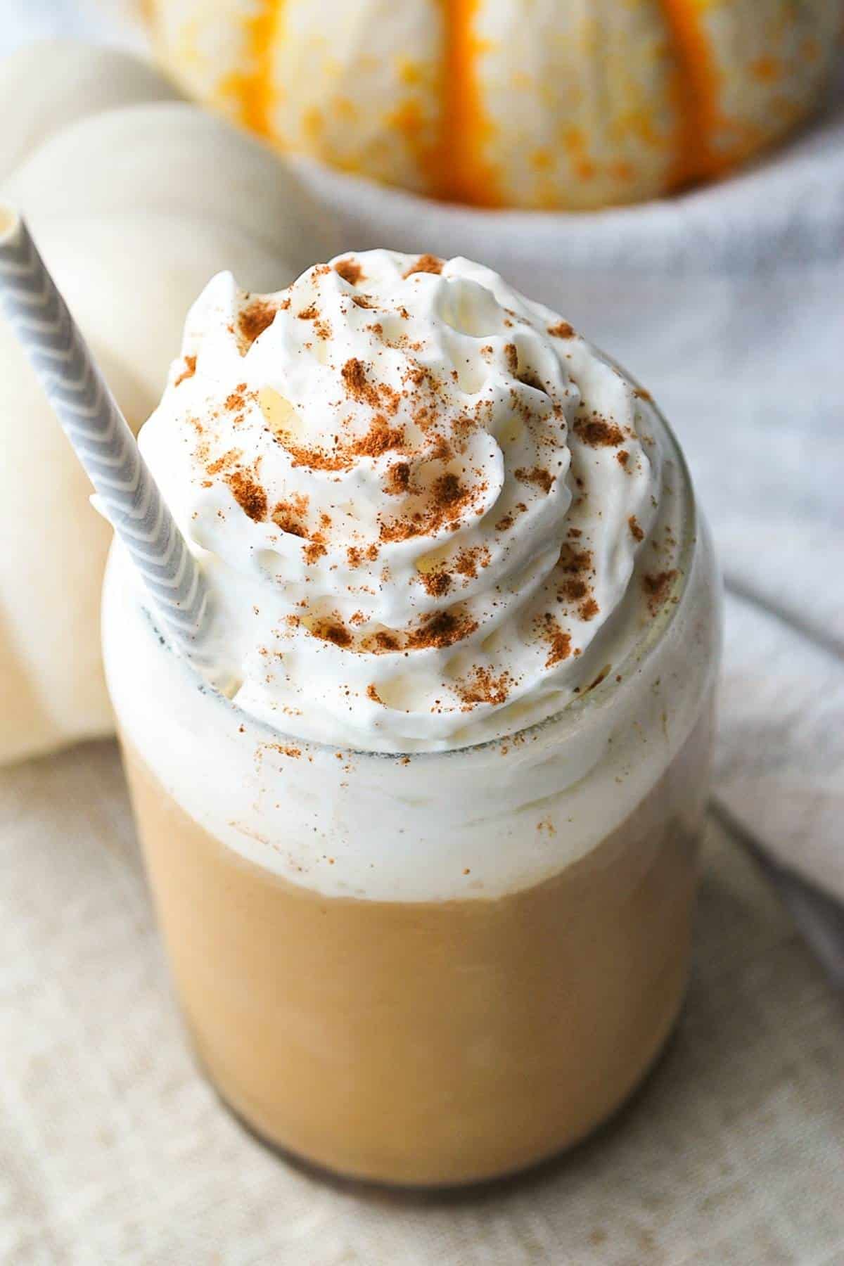 iced pumpkin spice latte topped with whipped cream and cinnamon with a paper straw