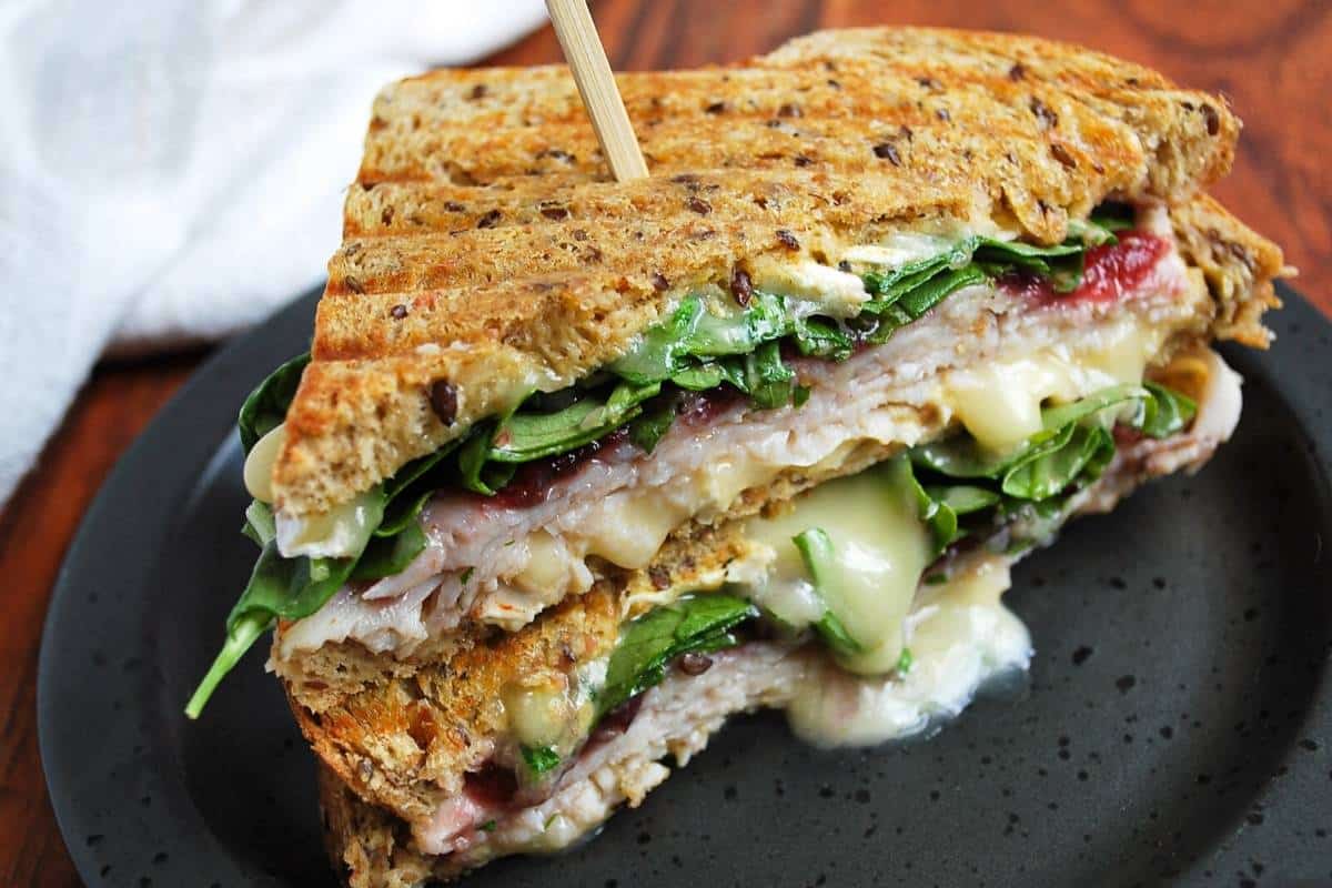 a turkey cranberry brie panini with arugula sliced in half with cheese oozing out the middle