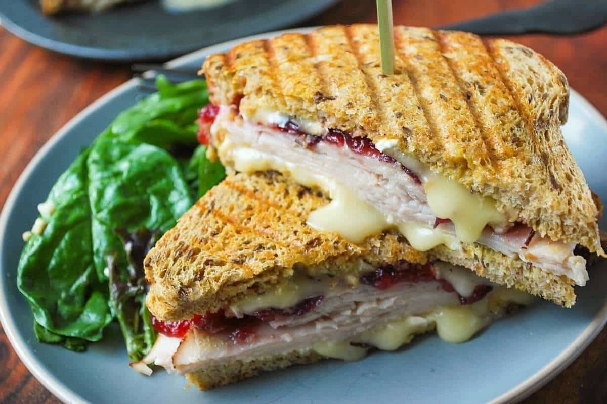 a turkey panini with brie cheese and cranberry sauce slice in half on a plate with salad. 