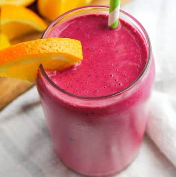 a glass of beet smoothie with frozen banana, berries, orange juice, yogurt, and beets with a napkin underneath