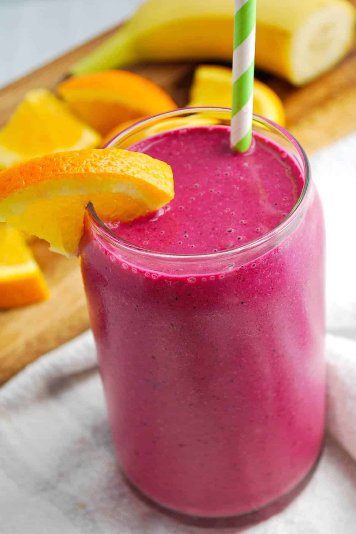 a magenta colored beet smoothie with an orange slice on the rim and green striped straw