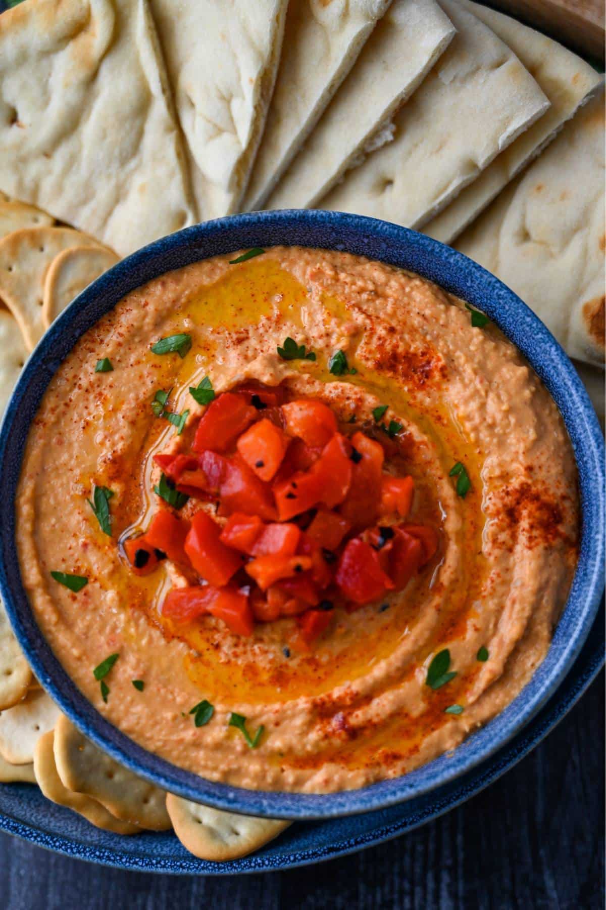 photo looking down at a bowl of fresh paprika hummus with pita slices and crackers