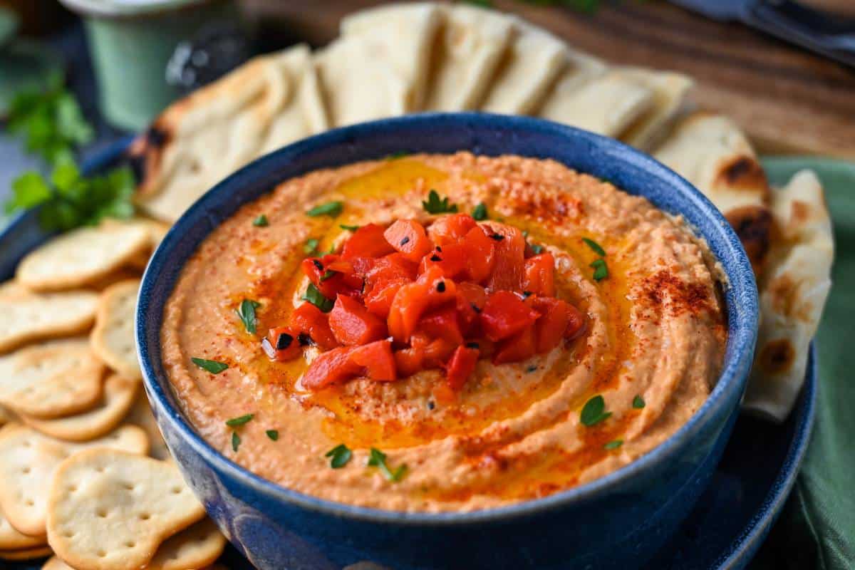 side view of a platter with a bowl of paprika hummus with fresh parsley and a jar of salt in the background