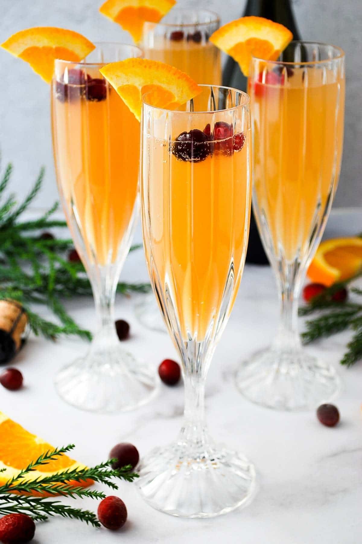 fresh cranberry prosecco mimosas in champagne flutes garnished with fresh orange and cranberries
