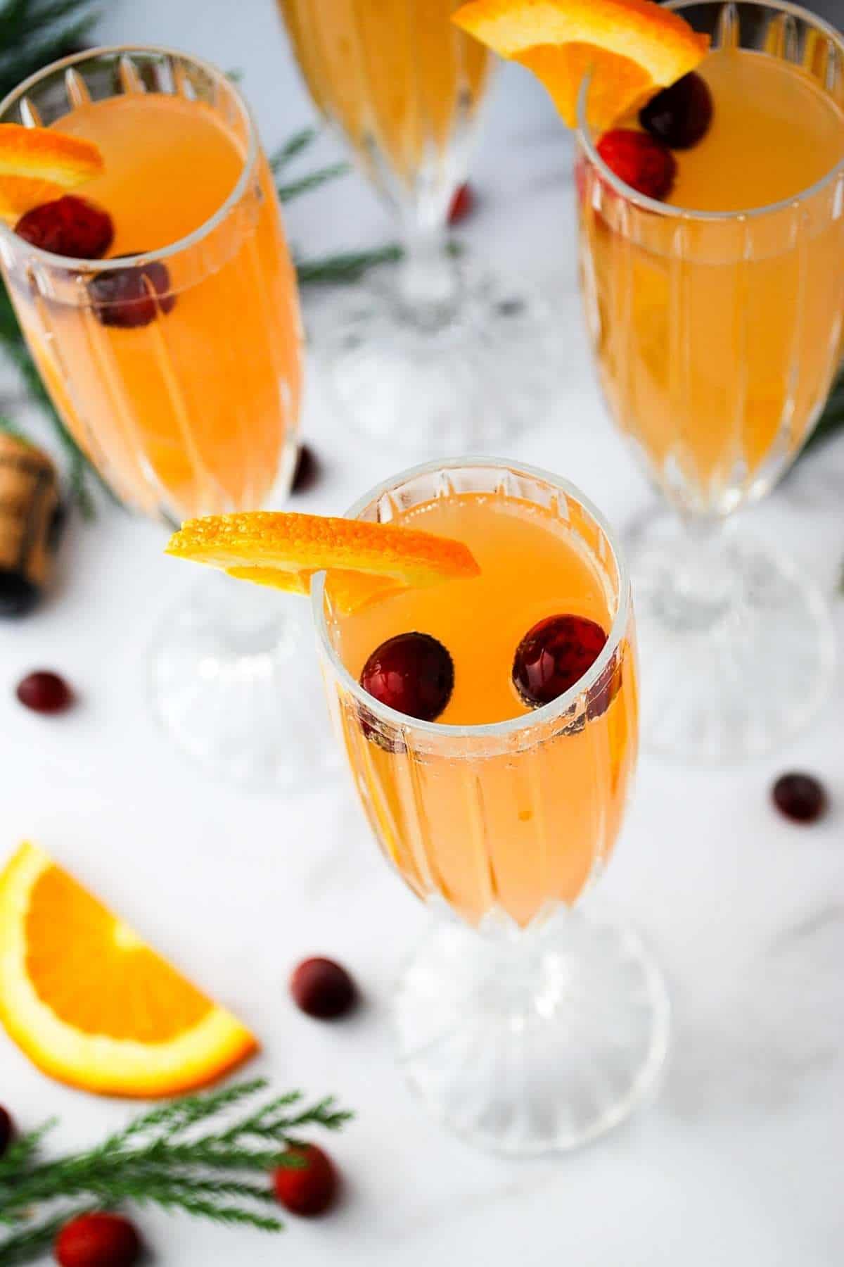 overhead photo of champagne flutes filled with mimosas and topped with fresh cranberries and an orange slice on the rim