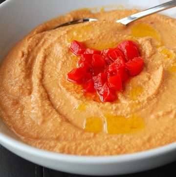 roasted red pepper hummus in a bowl with chopped roasted red peppers and a drizzle of olive oil on top