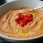 Red pepper hummus in a bowl with roasted red peppers on top