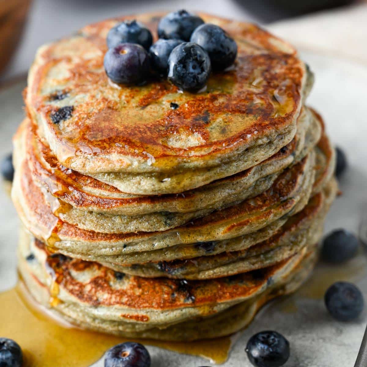dripping stack of blueberry oatmeal pancakes with maple syrup and blueberries