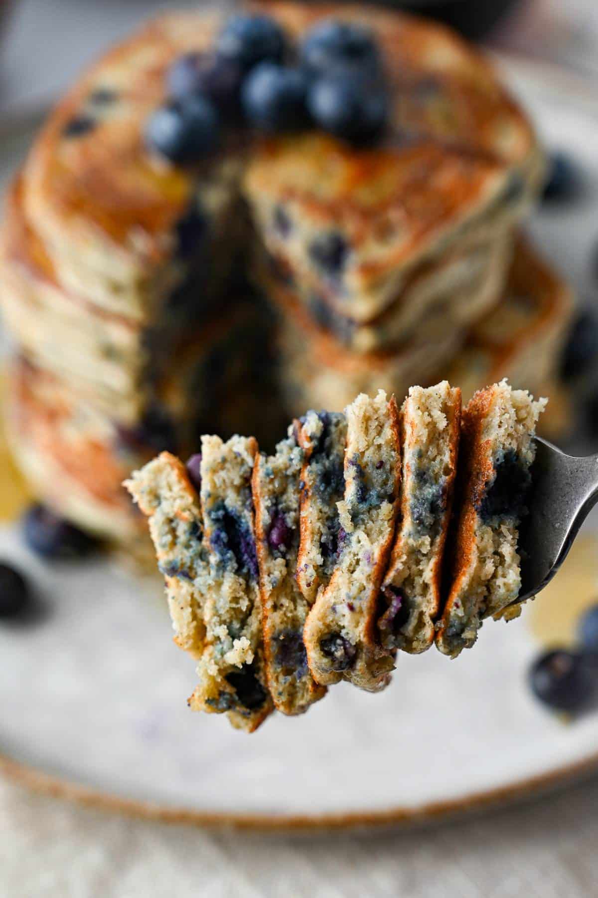 a stack of blueberry pancakes with a bite cut out with a fork