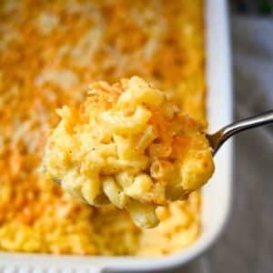 holding up a serving of mac and cheese over a casserole dish