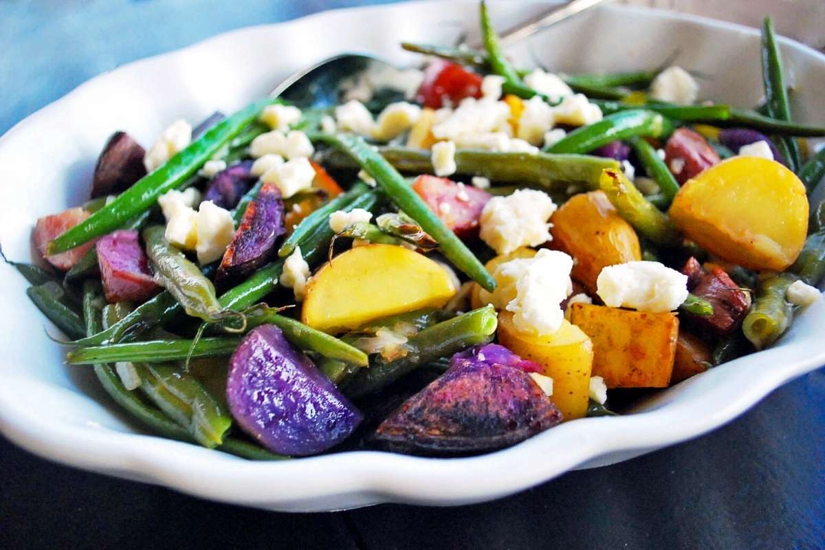 roasted potato salad with green beans and feta cheese in a white bowl