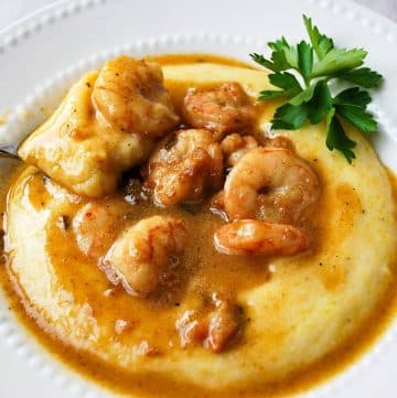 close up photo of a bowl of shrimp and grits with a spoon lifting up a bite