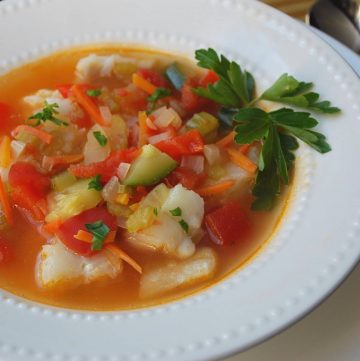 close up of a bowl of broth-based fish soup with a sprig of parsley on the side